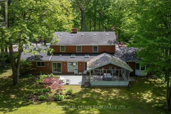 Aerial view of the rear exterior of a red brick house with a wooden deck and screened-in porch surrounded by trees. - 25 Riverside Drive, Kingston)