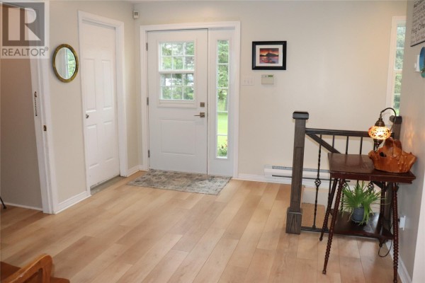 Interior view of a bright home entrance with light wood floors, a white door, and a decorative side table. - 25 Seaside Drive, Kippens