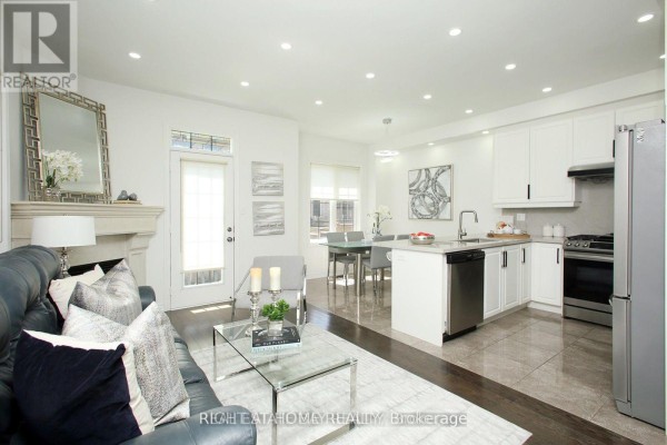 Open concept living and kitchen area with white cabinets, stainless steel appliances, and dining table. - 25 Sibella Way, Vaughan