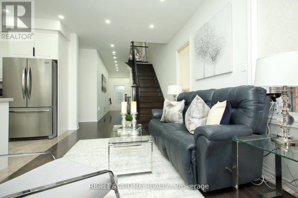 Living room looking down a hallway towards the stairs with a dark leather sofa and stainless steel fridge. - 25 Sibella Way, Vaughan