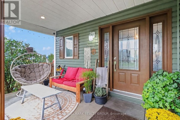Covered front porch with a swing chair, red sofa, coffee table, and front door. - 25 Tabitha Cres Crescent, North Dundas