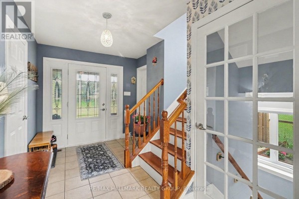 Interior view of a bright entryway with tiled floors, a wooden staircase, and glass-paneled doors. - 25 Tabitha Cres Crescent, North Dundas