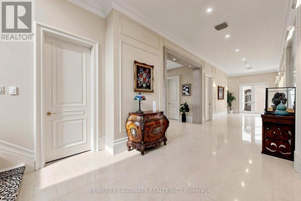 Long, wide hallway with cream-colored walls, white doors, decorative chest, and artwork. - 25 The Bridle Path, Toronto