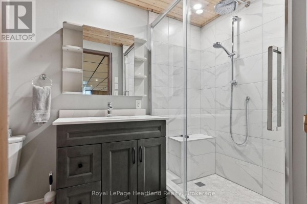 Modern bathroom with dark gray vanity, glass shower, and rain shower head - 25 Vincent Street South Bruce
