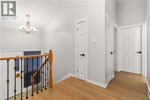 Interior hallway with light grey walls, wood flooring, and a wooden banister with black spindles. - 25 Vista Drive, Moncton