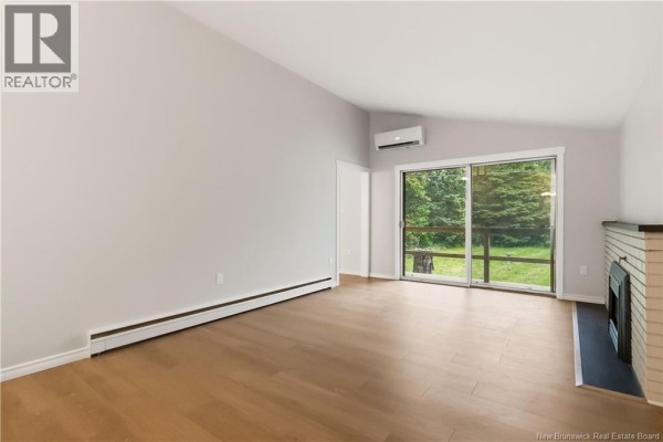 Living room with light grey walls, light wood flooring, and a sliding glass door overlooking a backyard. - 25 Vista Drive, Moncton