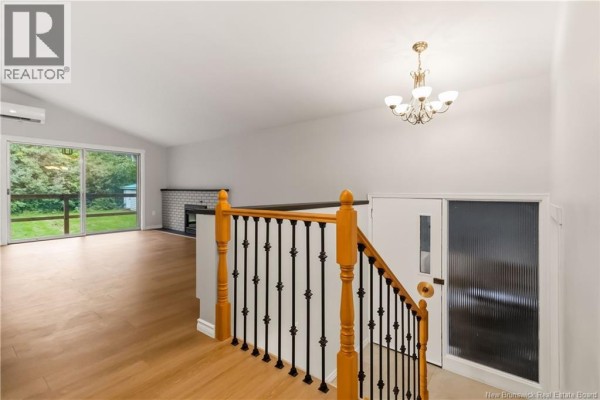 View from the hallway looking into the living room with a fireplace, vaulted ceiling, and staircase. - 25 Vista Drive, Moncton