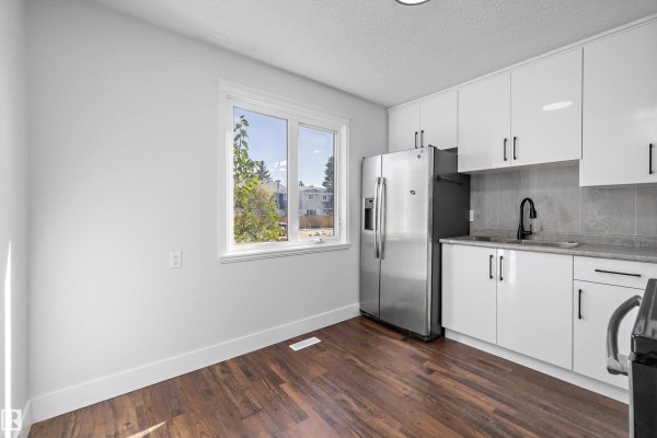 A kitchen area with white cabinets, stainless steel refrigerator, and a window overlooking trees. - 250 Callingwood Two Nw, Edmonton
