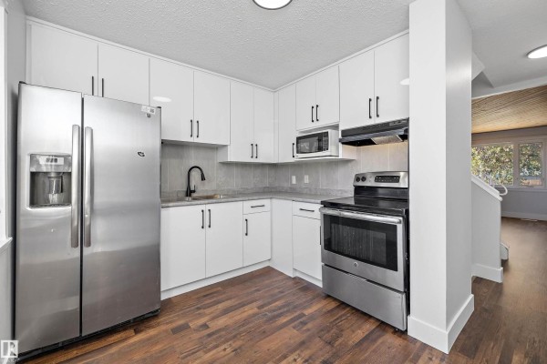 Kitchen with white cabinets, stainless steel appliances including refrigerator and stove, and wooden flooring. - 250 Callingwood Two Nw, Edmonton