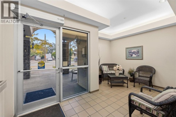 Apartment building lobby with beige walls, tiled floor, and wicker furniture. - 250 Dougall Road N Unit# 208, Kelowna