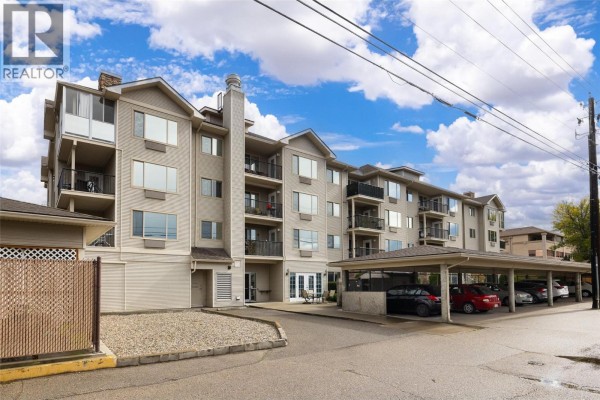 Exterior of a multi-story apartment building with covered parking and beige siding. - 250 Dougall Road N Unit# 208, Kelowna