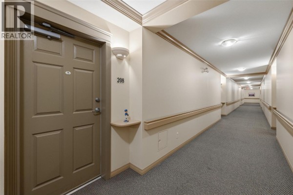 Hallway in apartment building with grey carpet, beige walls, and door 208. - 250 Dougall Road N Unit# 208, Kelowna