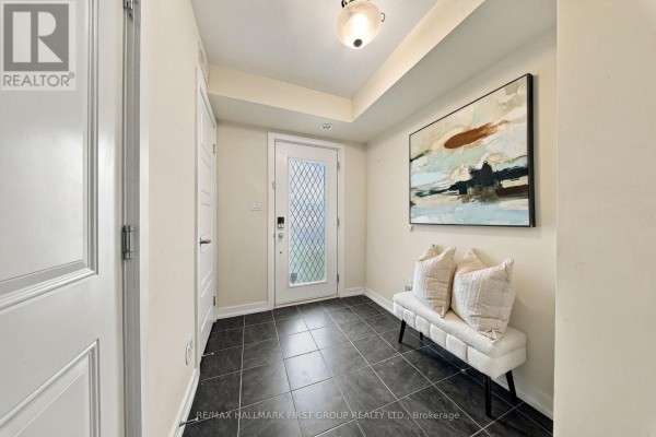 Foyer with dark tile flooring, white walls, a glass-paned front door, and a decorative bench. - 250 Finch Avenue, Pickering