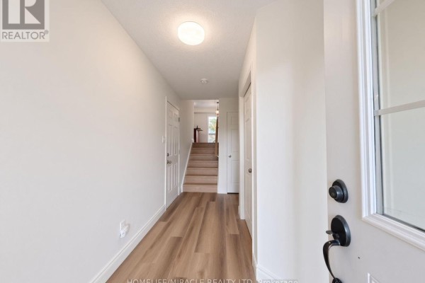 View from front door into a bright hallway with laminate flooring and stairs. - 250 Parkvale Drive, Kitchener