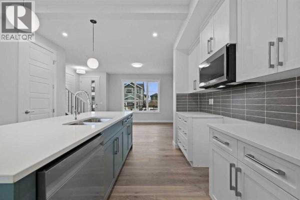 Modern kitchen with white cabinets, grey backsplash, stainless steel appliances, and island. - 250 Southbow Avenue, Cochrane