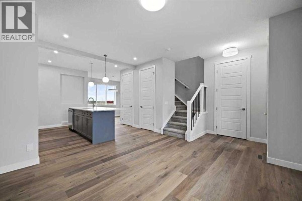 Open concept living space with kitchen island, stairs, and multiple doorways. - 250 Southbow Avenue, Cochrane