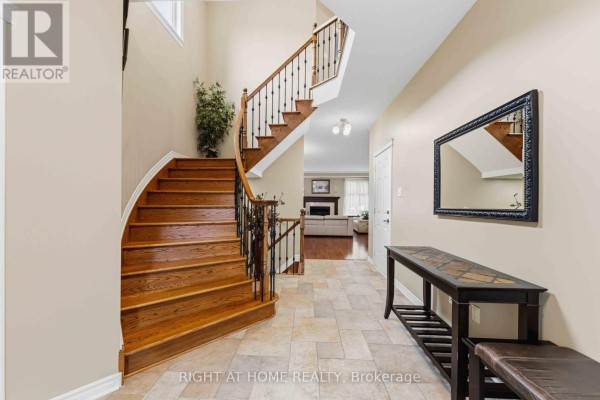 Interior foyer with curved wooden staircase, tiled floor, and console table. - 250 Tofino Private, Ottawa