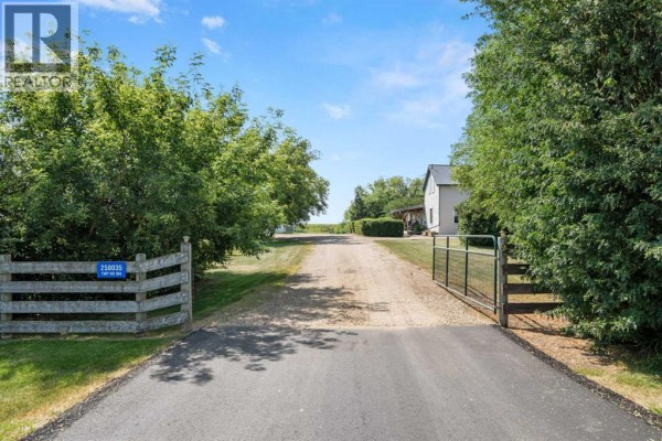 Gravel driveway leading to a gated entrance of a rural property with mature trees. - 250035 Township Road 304, Rural Kneehill County