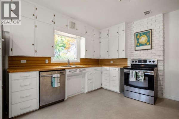 Kitchen with white cabinets, wooden countertops, stainless steel appliances, and a brick accent wall. - 2501 20 Street, Nanton