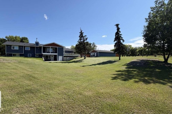 Rear view of a dark blue home with white trim and trees on a grassy lawn. - 25032 Richfield Rd, Rural Sturgeon County