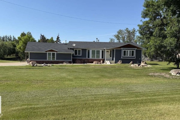 Front exterior of a single-story home with dark blue siding and many windows. - 25032 Richfield Rd, Rural Sturgeon County