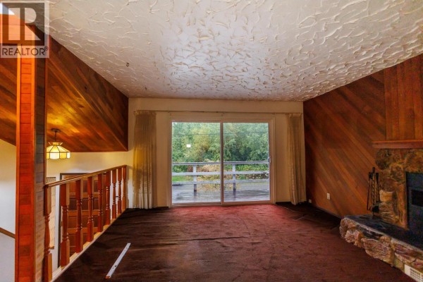 Living room with a stone fireplace, wood paneling, and view of a deck. - 2504 Kerr Street, Terrace