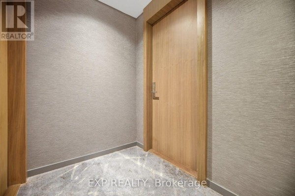 Hallway with textured wallpaper and a wooden door leading to a condo unit. - 2505 - 200 Bloor Street W, Toronto