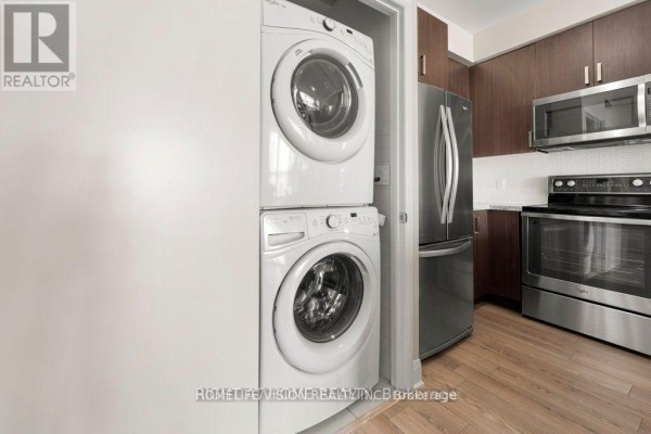 Stacked white front-load washing machine and dryer next to a stainless steel refrigerator. - 2505 - 2900 Hwy 7, Vaughan