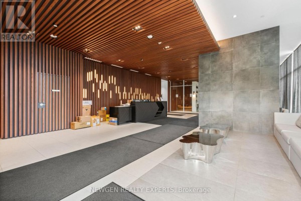 Apartment building lobby with a dark reception desk, wooden slat walls, and grey tiled floors. - 2505 - 297 Oak Walk Drive, Oakville