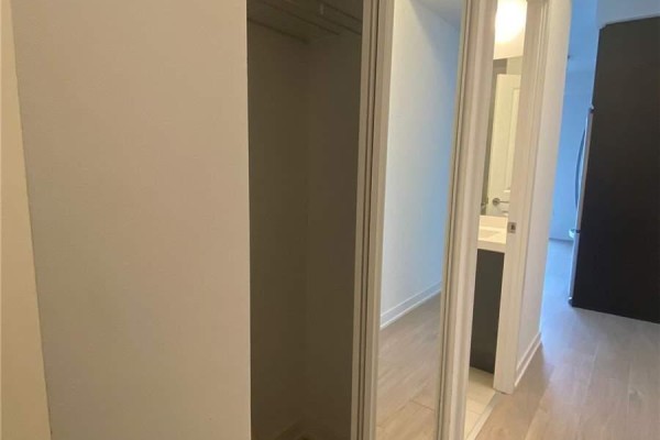 A closet with mirrored sliding doors and a hallway with light wood flooring. - 2506 - 8 Nahani Way, Mississauga