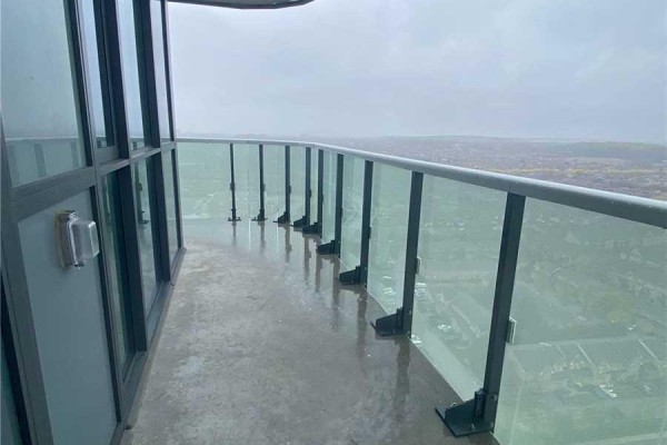 A large balcony with a glass railing and a city view on a cloudy day. - 2506 - 8 Nahani Way, Mississauga