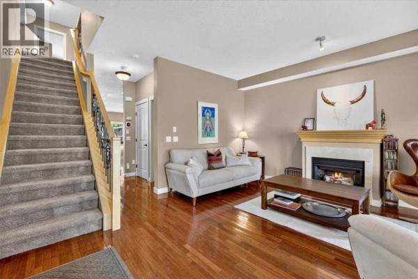 Living room with hardwood floors, a gas fireplace, and a staircase with carpeted steps. - 2506 17 Street Se, Calgary