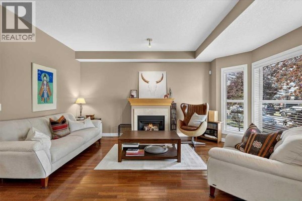 Living room with hardwood floors, a gas fireplace, and large windows overlooking the street. - 2506 17 Street Se, Calgary