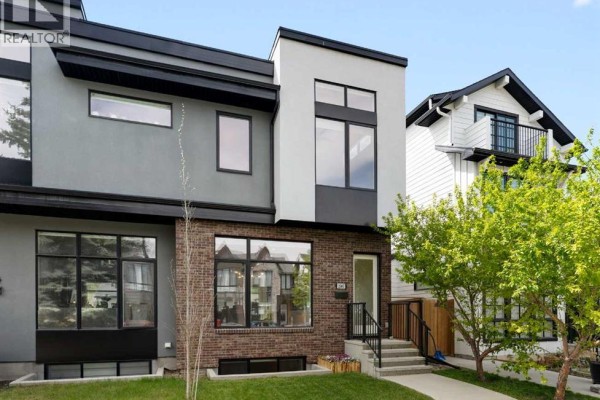 Front exterior of a duplex with grey stucco, brick, and large windows. - 2507 17 Street Nw, Calgary