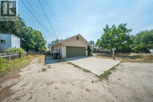 Side view of the house and driveway, with a large green garage door and surrounding trees. - 2507 Columbia Avenue, Castlegar