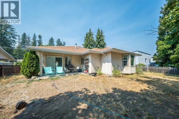 Backyard view of the house with a patio, lawn chairs, and a fenced yard with trees. - 2507 Columbia Avenue, Castlegar