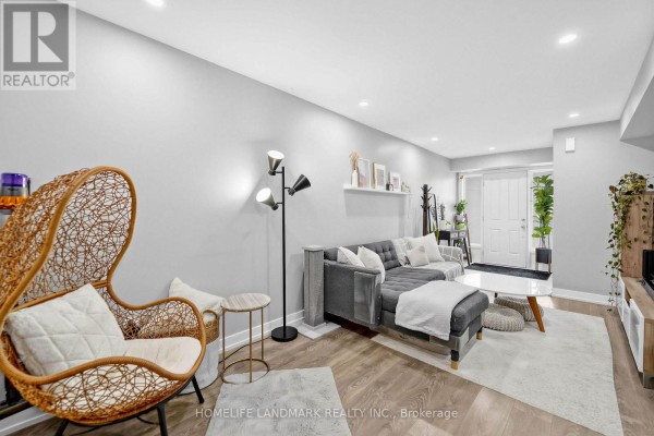 Living room with grey sofa, rattan hanging chair, and floor lamp, showing entrance to the backyard. - 251 - 60 Parrotta Drive, Toronto