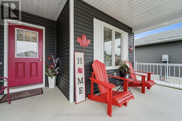 Covered front porch with two red Adirondack chairs, a welcome mat, and decorative items. - 251 Lake Breeze Drive, Ashfield Colborne Wawanosh