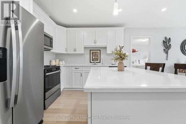 A modern kitchen with white cabinets, stainless steel appliances, and a large island with white countertops. - 251 Lake Breeze Drive, Ashfield Colborne Wawanosh