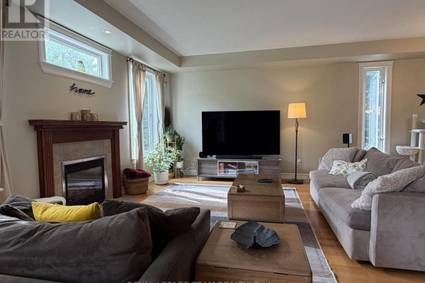 Living room with a fireplace, television, two sofas, and wooden coffee tables. - 251 Tofino Private, Ottawa
