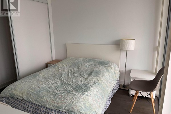 Bedroom with a queen-size bed, white headboard, wooden nightstand, and a floor lamp. - 2510 - 57 St. Joseph Street, Toronto