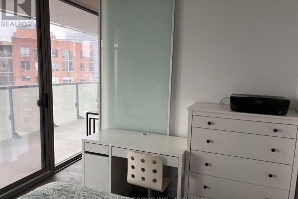A white desk and printer sit on a dresser next to a frosted glass partition and balcony door. - 2510 - 57 St. Joseph Street, Toronto