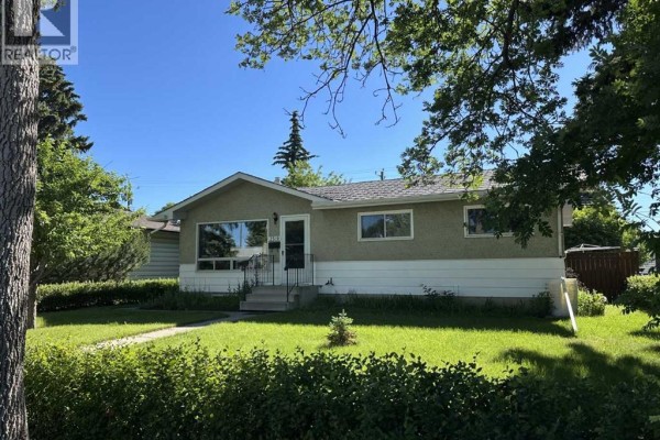 Side exterior view of a light green and white bungalow with trees in the foreground. - 2510 35 Street Se, Calgary