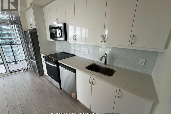 Modern kitchen with white cabinetry, stainless steel appliances, and light gray tiled backsplash. - 2511 - 38 Annie Craig Drive, Toronto