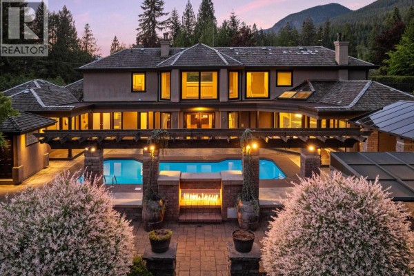 Evening view of the home's backyard with a lit swimming pool, outdoor fireplace, and manicured landscaping. - 2514 East Road, Anmore