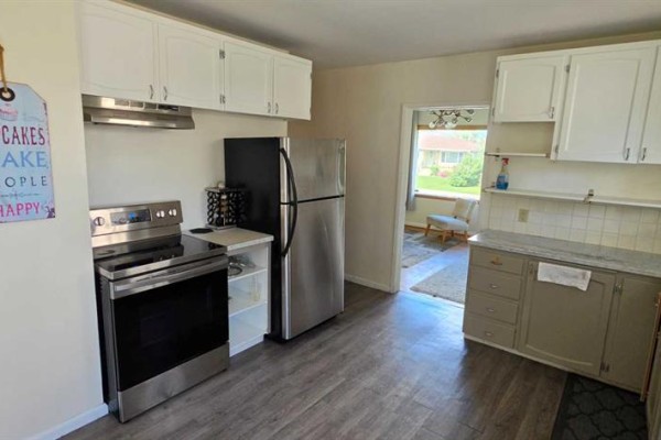 Kitchen with stainless steel appliances, a refrigerator, white cabinets, and a doorway to another room. - 2515 Cochrane Road Nw, Calgary