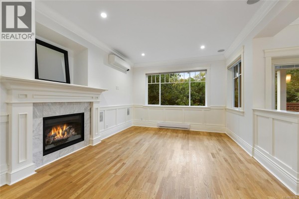 Living room with hardwood floors, a gas fireplace, wainscoting, and windows overlooking trees. - 2517 Asquith St, Victoria