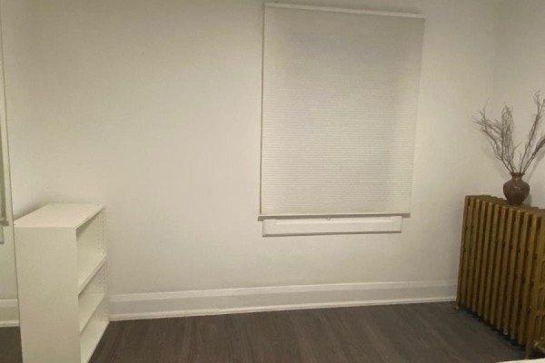 Corner of a room with a white bookshelf, large window with blinds, and wooden radiator. - 2518 Lake Shore Boulevard, Toronto