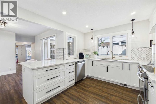 Modern white kitchen with island, stainless steel appliances, and dark wood floors. - 252, 20 Midpark Crescent Se, Calgary