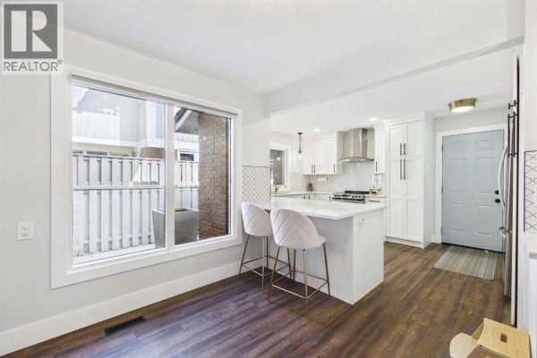 Bright kitchen area with island, stools, large window, and entryway. - 252, 20 Midpark Crescent Se, Calgary